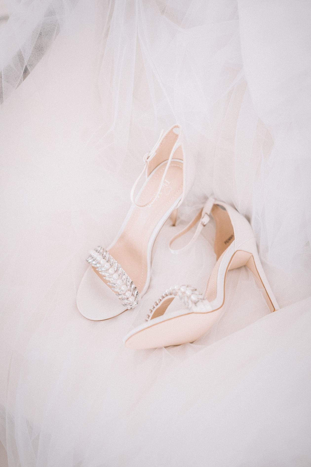 Ivory pearl-embellished bridal heels resting on a soft white veil